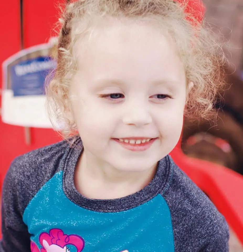 Close-up portrait of a smiling young child with curly light hair wearing a blue shirt.