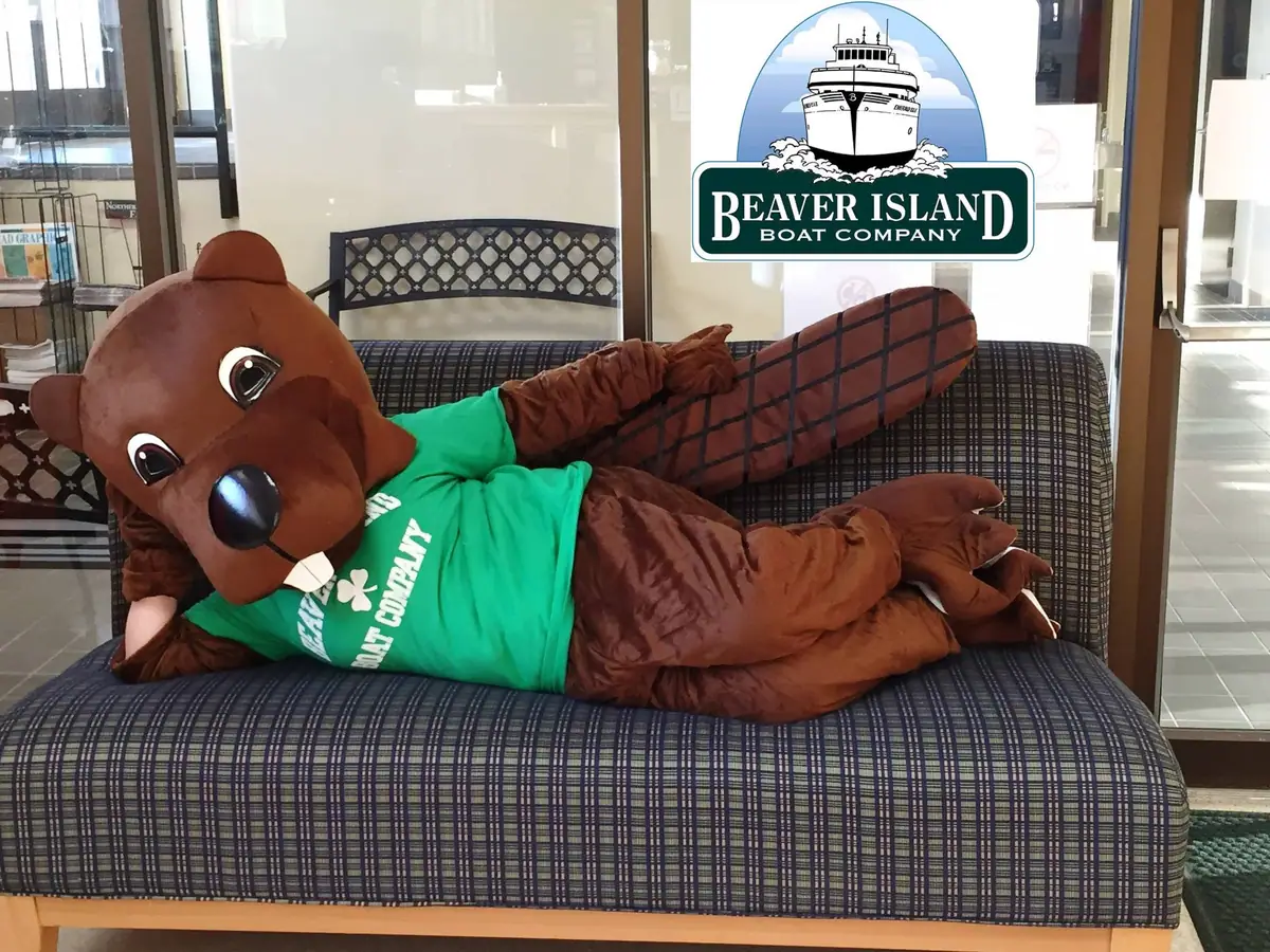 A beaver mascot in a green shirt reclines on a patterned couch beneath a boat-company logo.