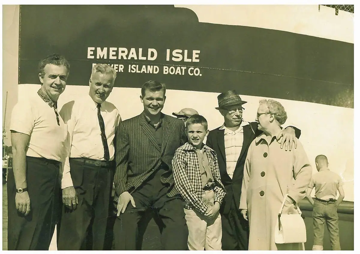 Adults and a boy pose beside a large vessel marked “EMERALD ISLE.”