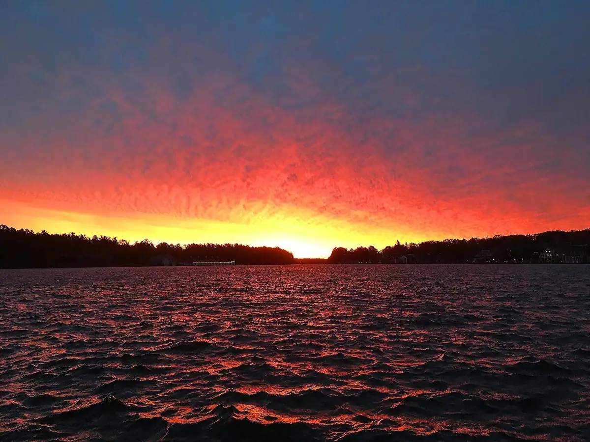 Sunrise glows over rippling water and a dark, tree-lined shoreline.
