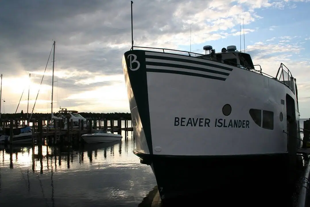 A large white ferry is moored beside a pier at sunset, with sailboats and reflections in the water.