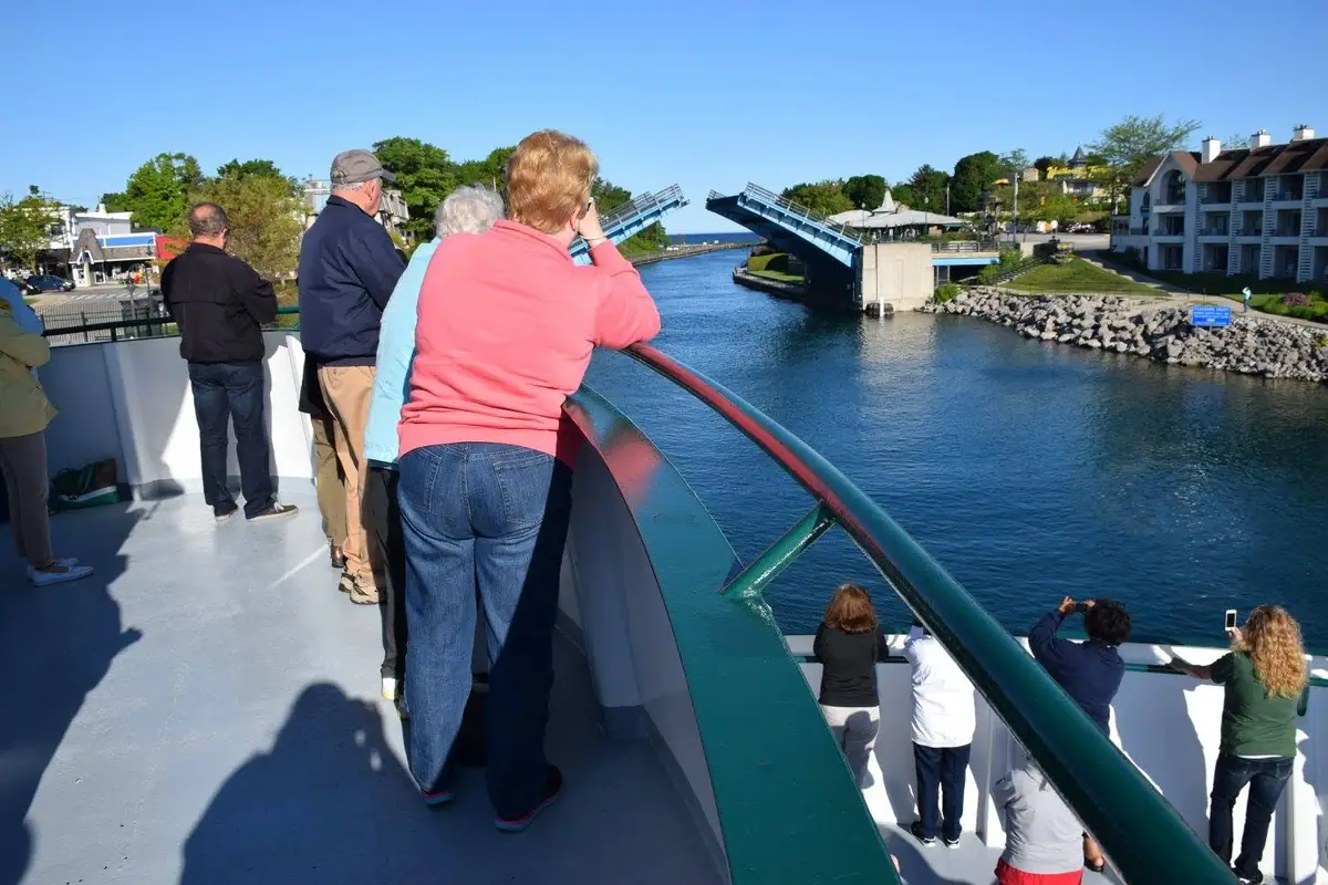 Passengers on a ferry watch a raised drawbridge over a waterway.