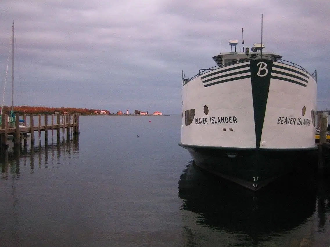 A large white ferry with black stripes is moored beside a wooden pier under a cloudy sky.