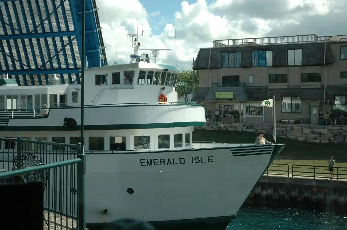 White passenger ferry with a green stripe docked beside a waterfront building and pier.