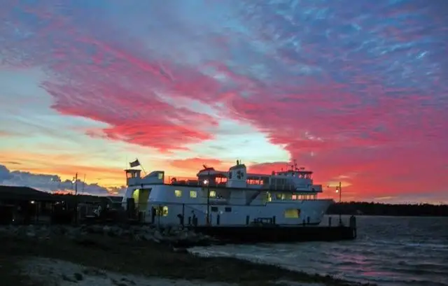 A white ferry sits beside a pier beneath vivid red and orange sunset clouds.