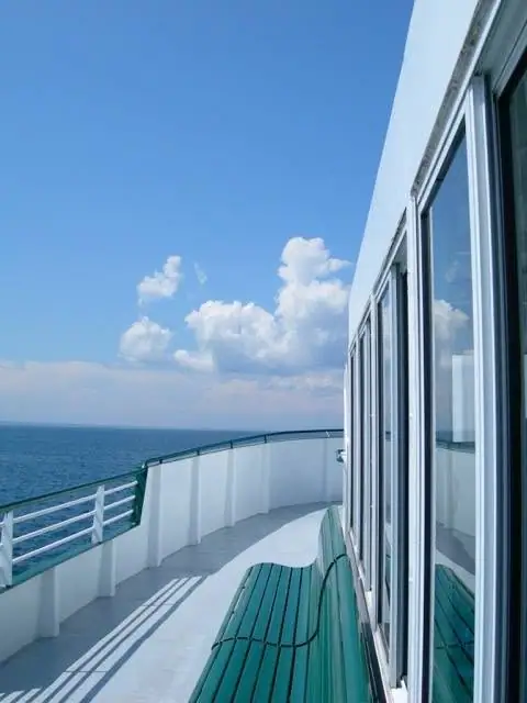 Passenger vessel deck with green benches, white railings, windows, open water, and cumulus clouds.