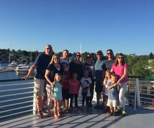 Adults and children pose together on a boat deck overlooking a marina.