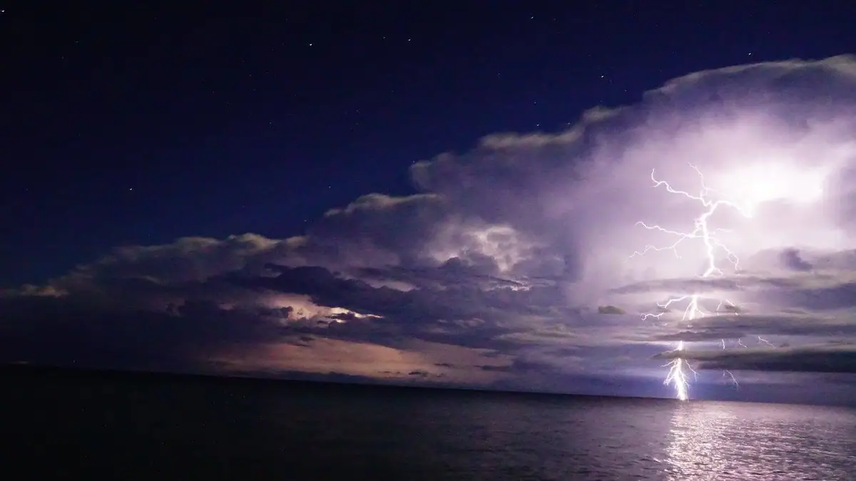 Lightning flashes over dark water beneath towering storm clouds at night.