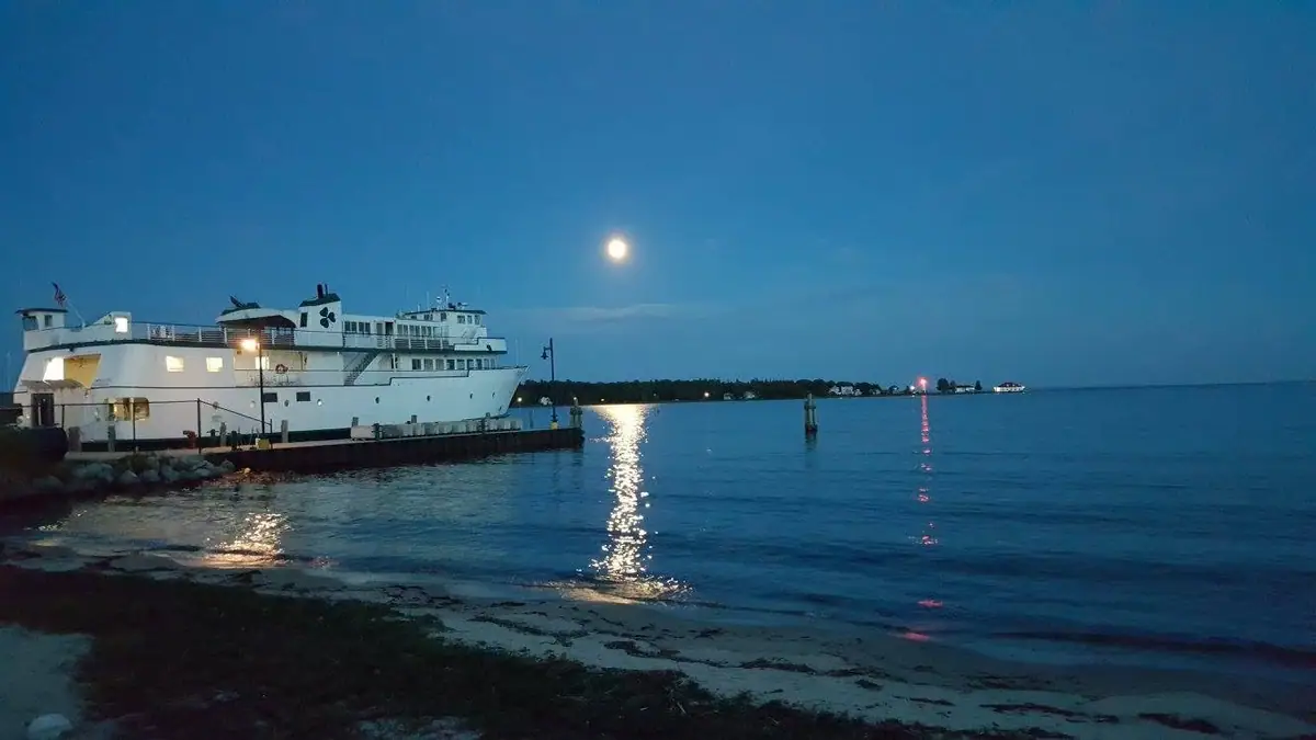 A white ferry sits beside a pier at night as moonlight reflects across the water.