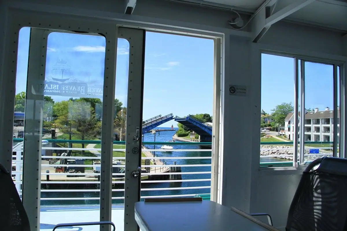 View from a vessel cabin toward a raised blue drawbridge, waterway, waterfront buildings, and a small boat.