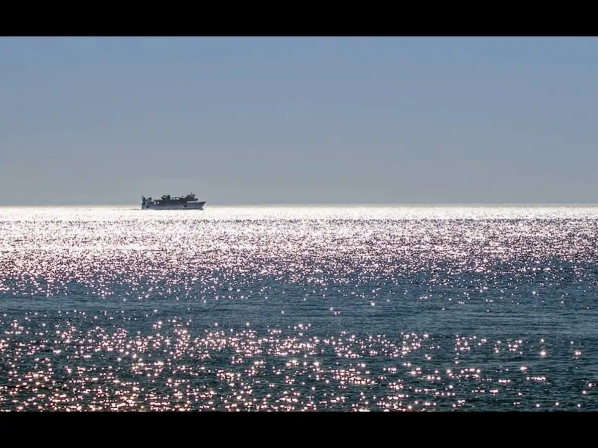 A distant ferry crosses bright, rippling water beneath a clear blue sky.