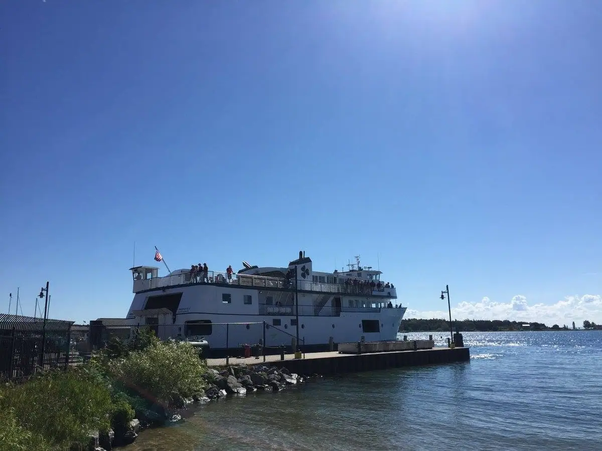 A white passenger ferry with people aboard is docked beside a pier on a sunny day.