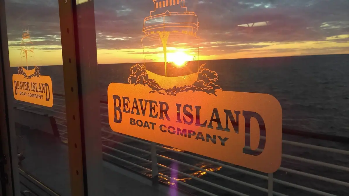 Orange boat-company decal on a window, with a ferry illustration silhouetted against a sunset over open water.