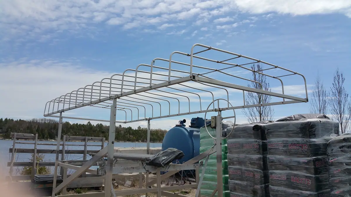 A galvanized metal framework stands beside a blue tank and stacks of plastic-wrapped BACCTO growing medium.