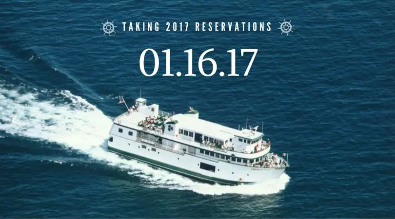 A white passenger ferry with green trim travels through dark blue water, leaving a broad white wake.
