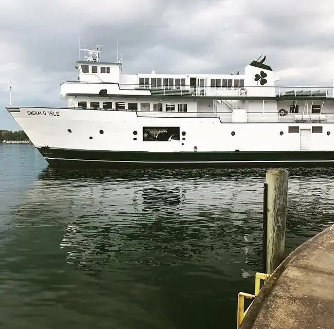 White passenger ferry with a dark green stripe and shamrock emblem beside a pier.
