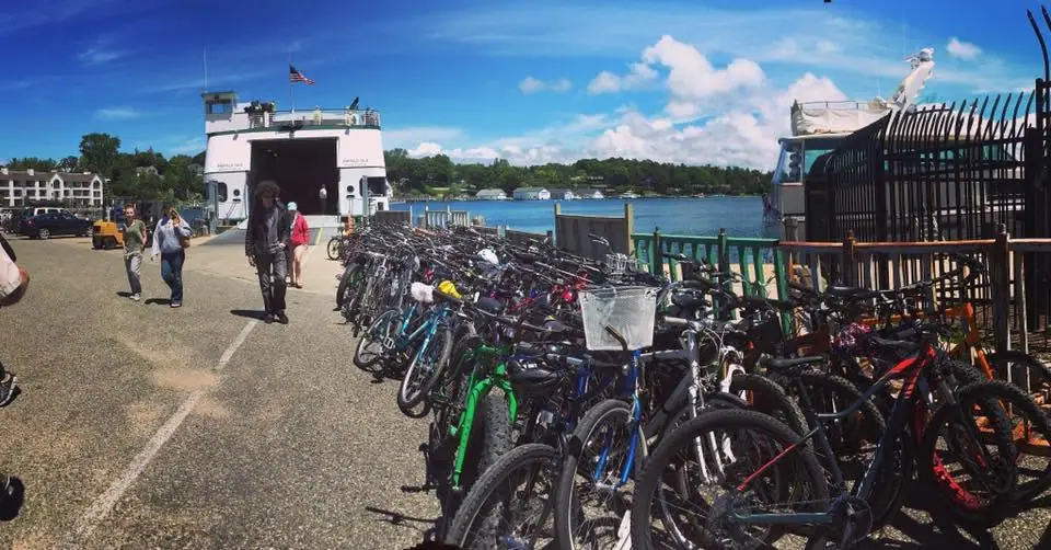 A white ferry stands at a dock beside a dense row of bicycles and several pedestrians.