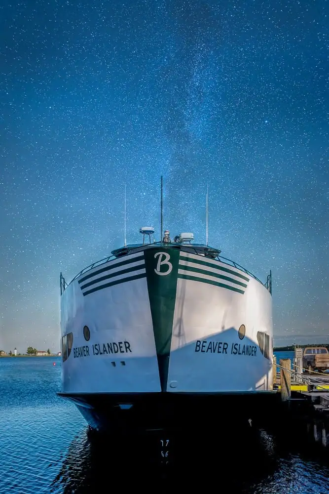 A white ferry with green stripes is moored bow-first at a dock beneath a star-filled sky.