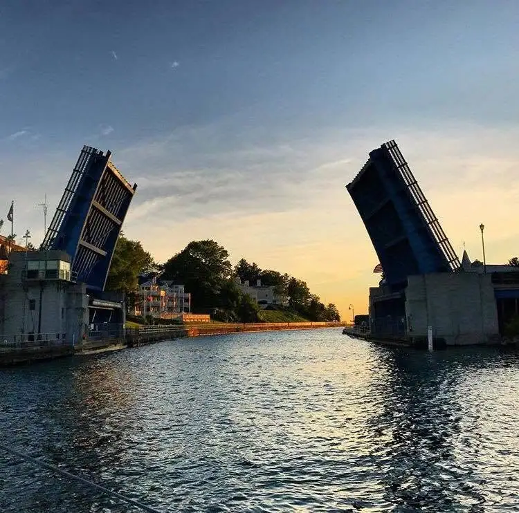 A raised drawbridge spans a waterway at sunset, with rippling water in the foreground.