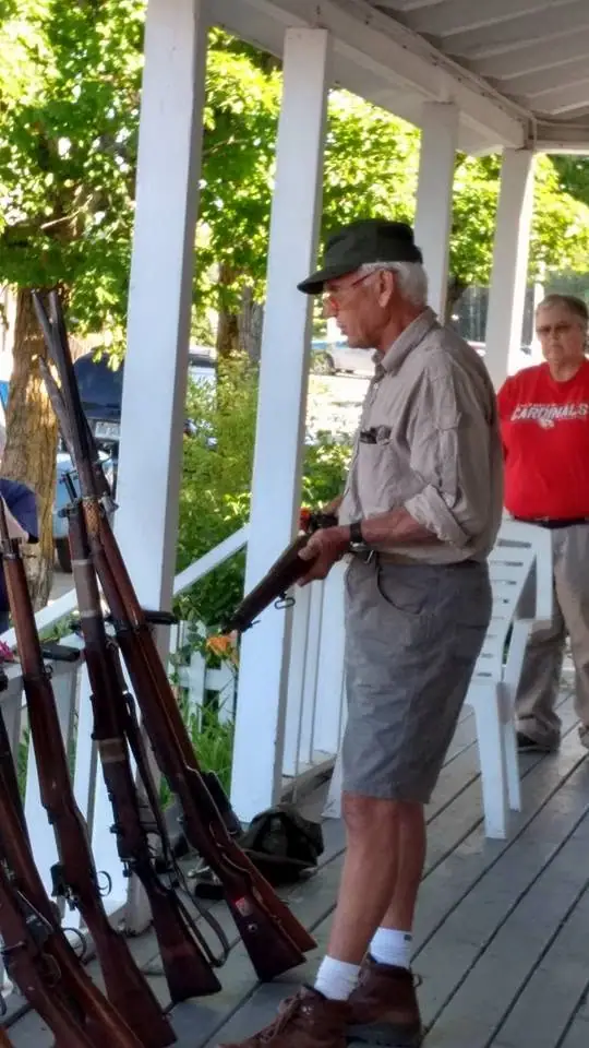 Two people stand on a porch beside several rifles, with the word “CARDINALS” visible on a sweatshirt.