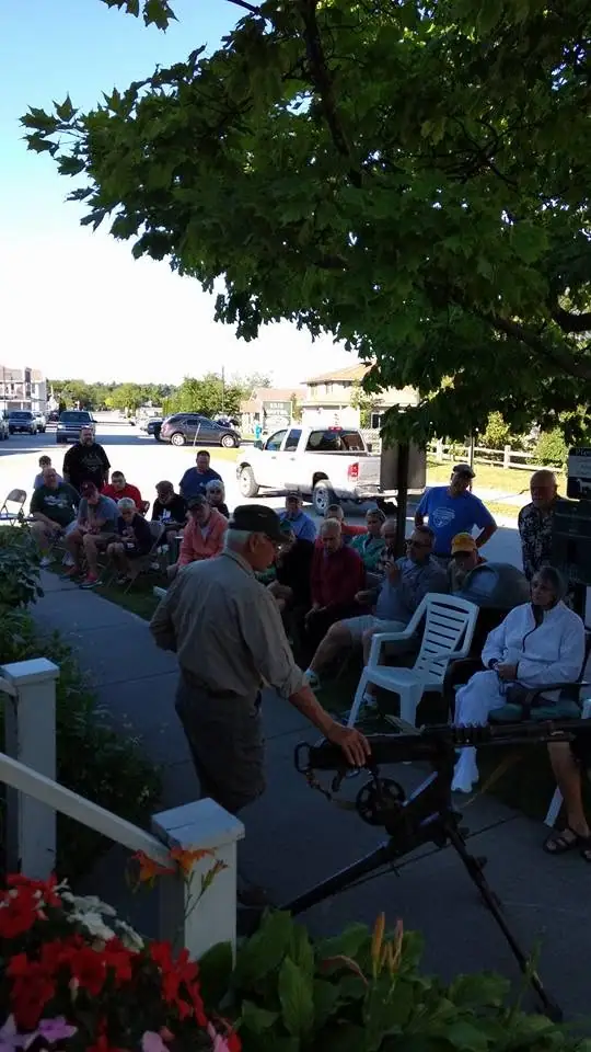 A man operates a large camera beside seated attendees at an outdoor talk.