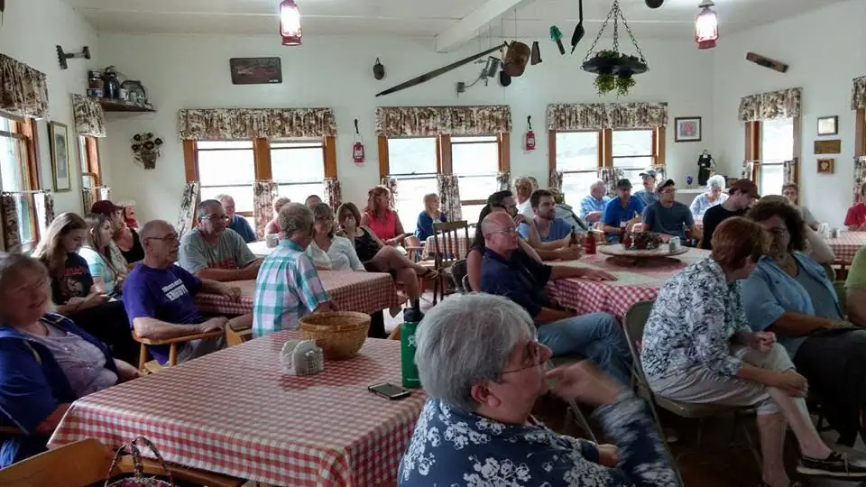 A large group sits at checkered tables in a bright rustic dining room.