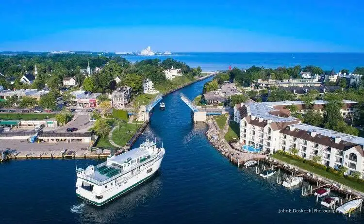 Aerial view of a green-striped ferry entering a channel beside waterfront buildings and docks.