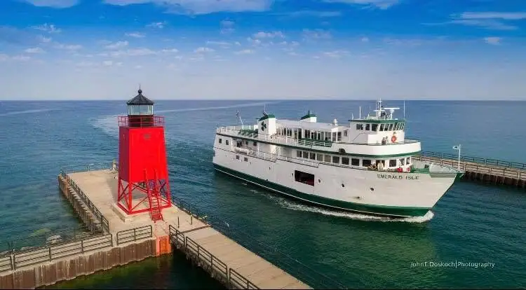 A white passenger ferry passes a bright red lighthouse at the end of a pier.