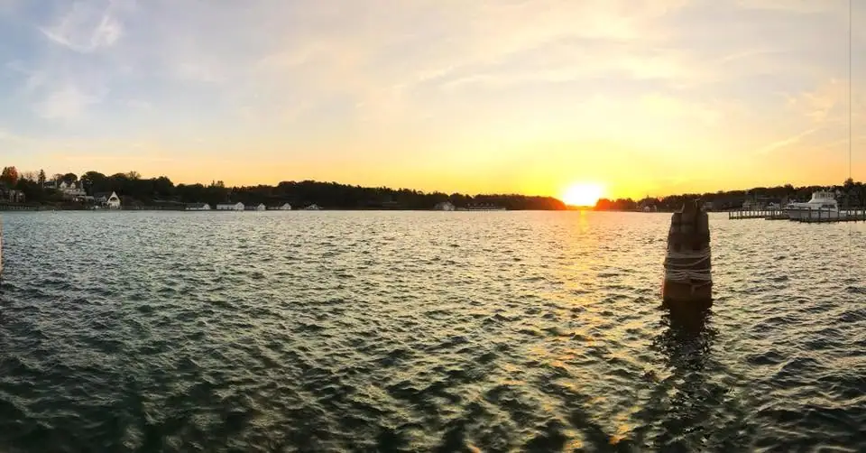 Sunset over rippling water with shoreline homes, docks, and a banded wooden mooring post.