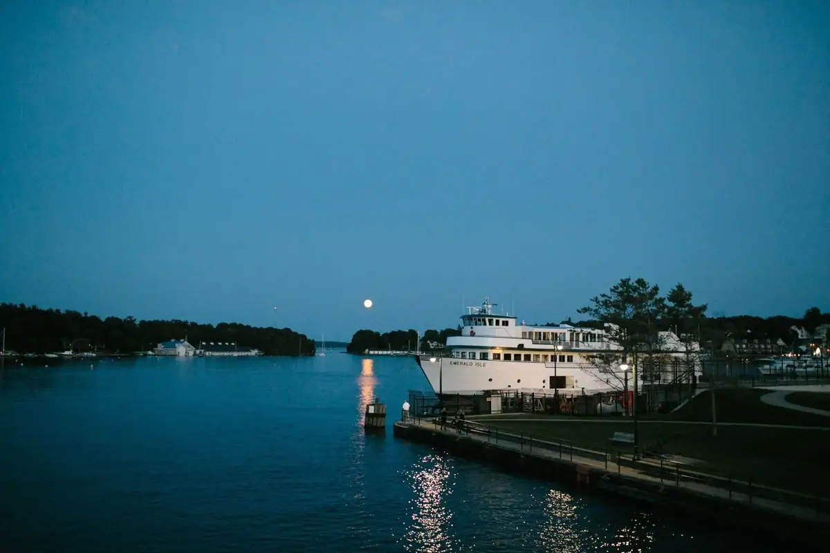A white passenger ferry is docked beside a waterfront promenade under a bright moon.