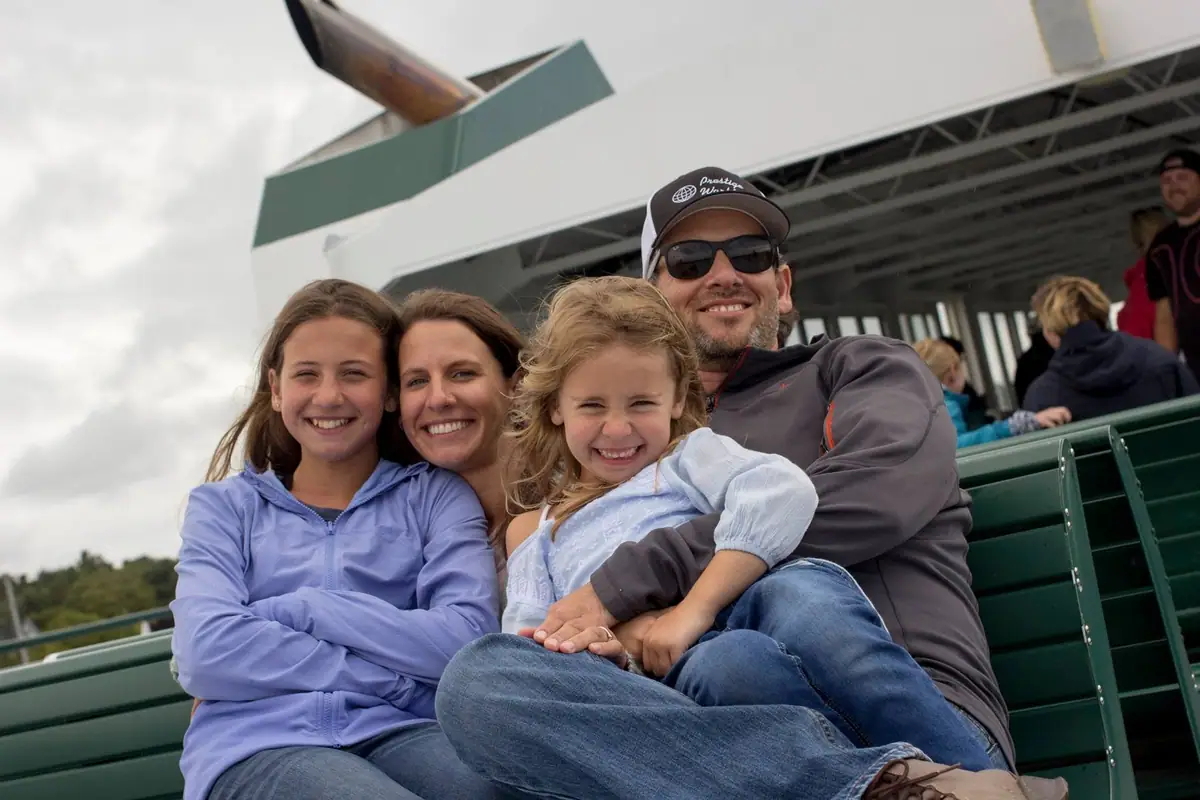 Four people smile together on green passenger benches aboard a ferry.