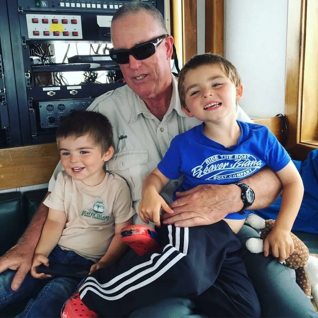A man wearing sunglasses sits with two young boys inside an equipment-filled interior.