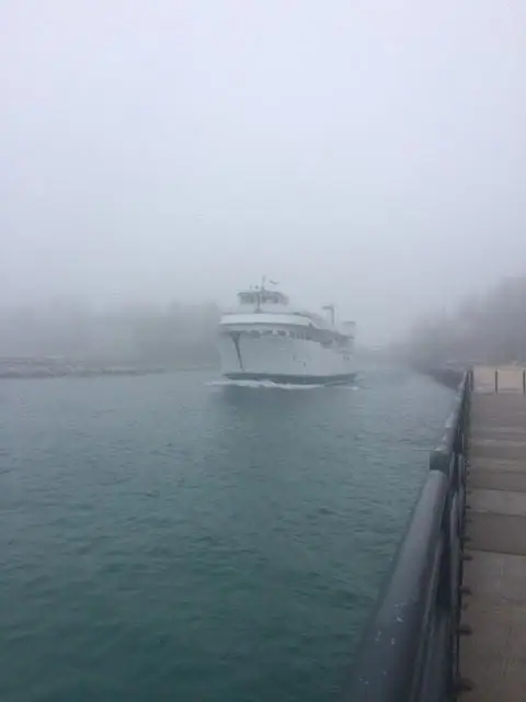 A white passenger ferry approaches along a foggy channel beside a dock with metal railings.