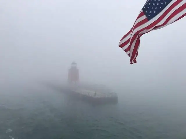 A lighthouse and pier fade into dense fog beneath a large American flag.