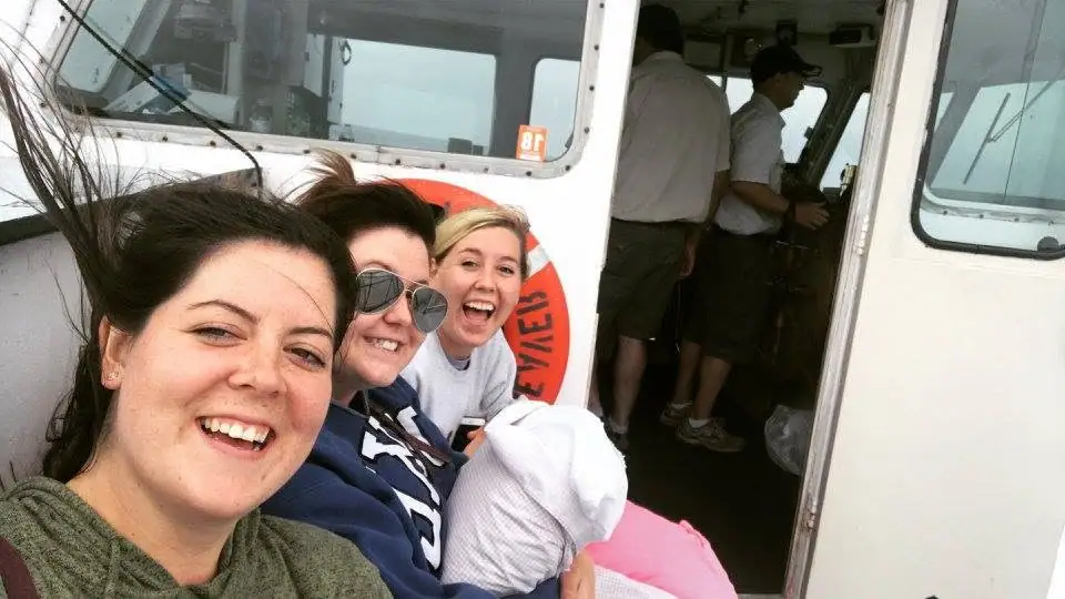Three women pose with a bundled infant beside an open passenger-vessel cabin while two men stand inside.