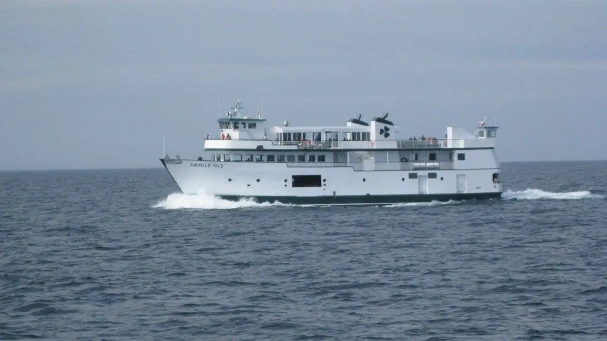 A white multi-deck ferry travels across choppy open water under an overcast sky.