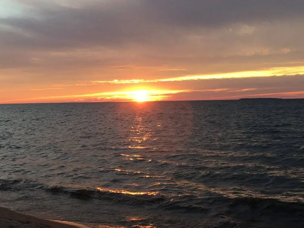 Sunset over rippling water, with a narrow sandy shoreline in the foreground.