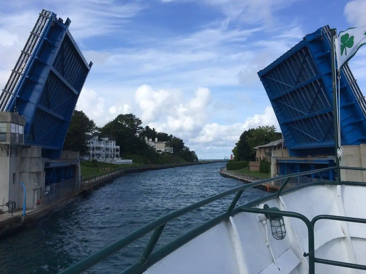 A boat passes between two raised blue drawbridges on a narrow waterway.