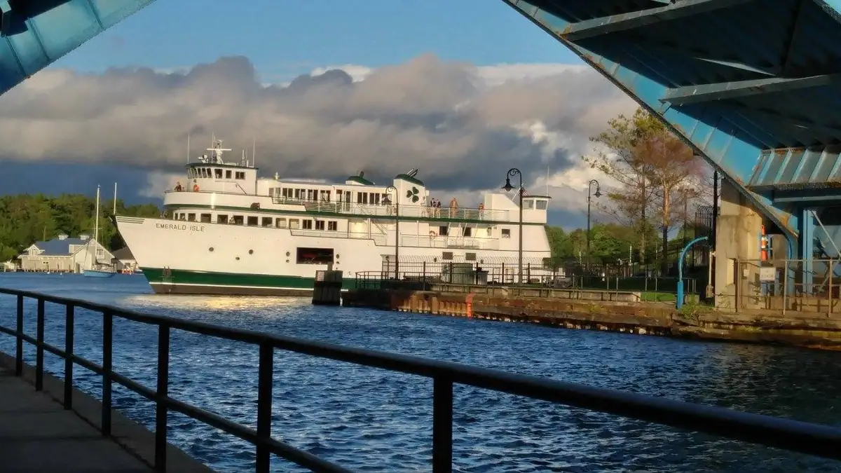 White passenger ferry beside a dock, viewed through a blue steel bridge under dramatic clouds.