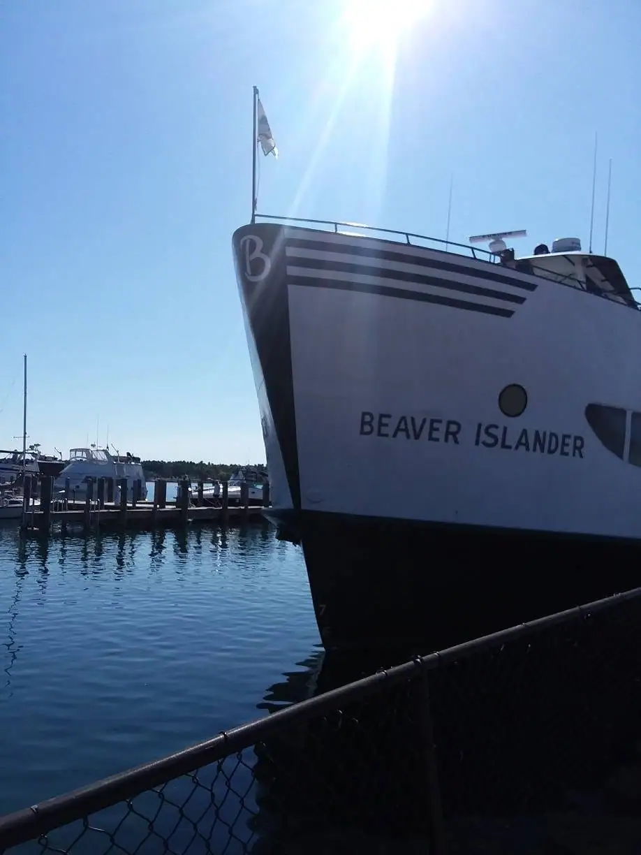 The bow of the ferry BEAVER ISLANDER beside a dock, with other boats and a chain-link fence visible.