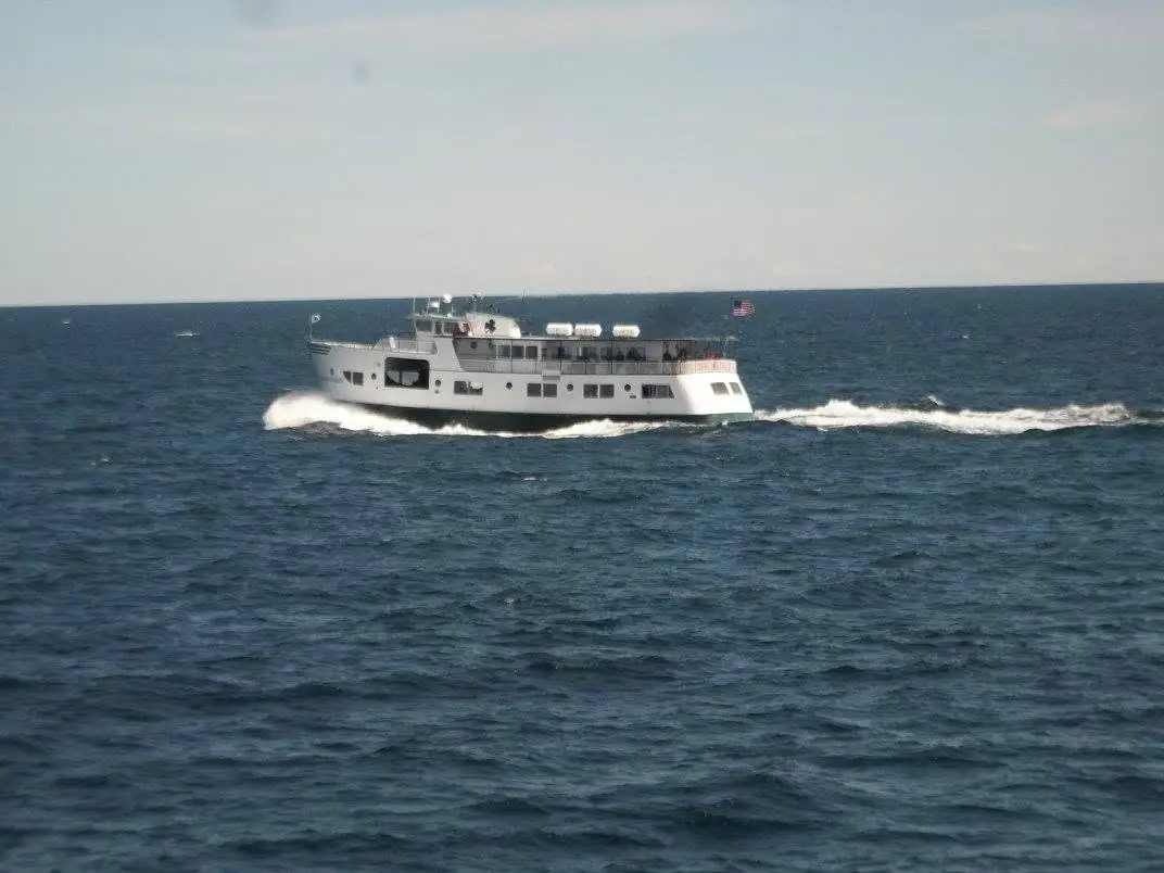 A white multi-deck ferry travels across dark blue water, leaving a foamy wake.