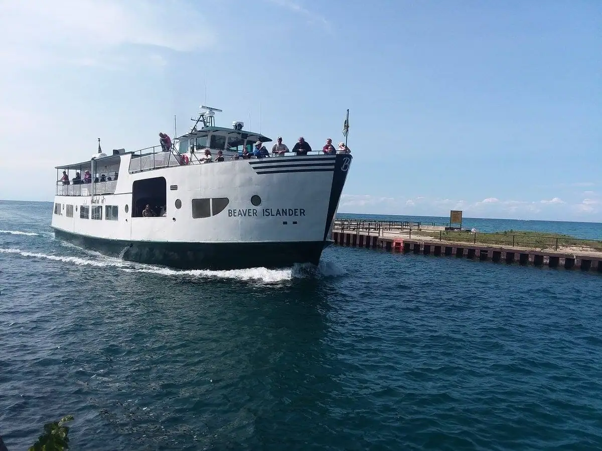 A white passenger ferry passes a pier with people gathered on its upper decks.