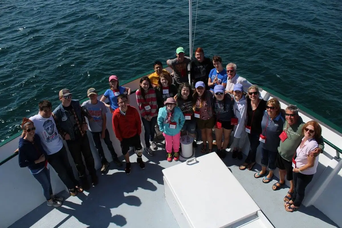 A group of adults and children pose together on a boat deck above open water.