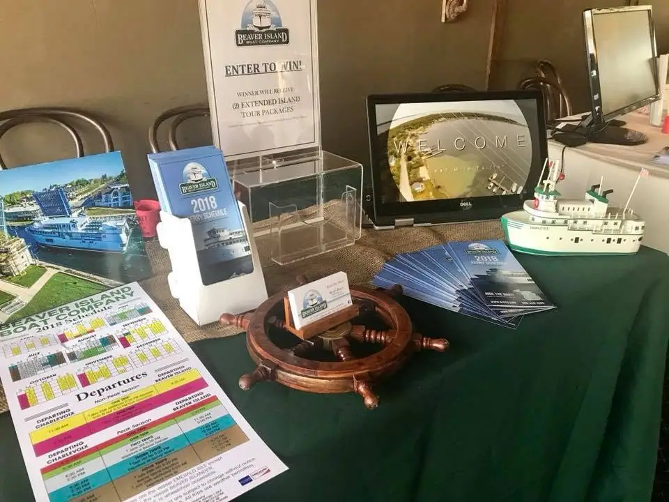 Promotional table display with ferry schedules, brochures, a ship wheel, and a model vessel.