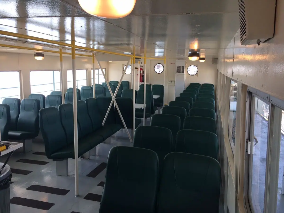 Interior of a passenger ferry with rows of dark green seats, yellow rails, and round windows.