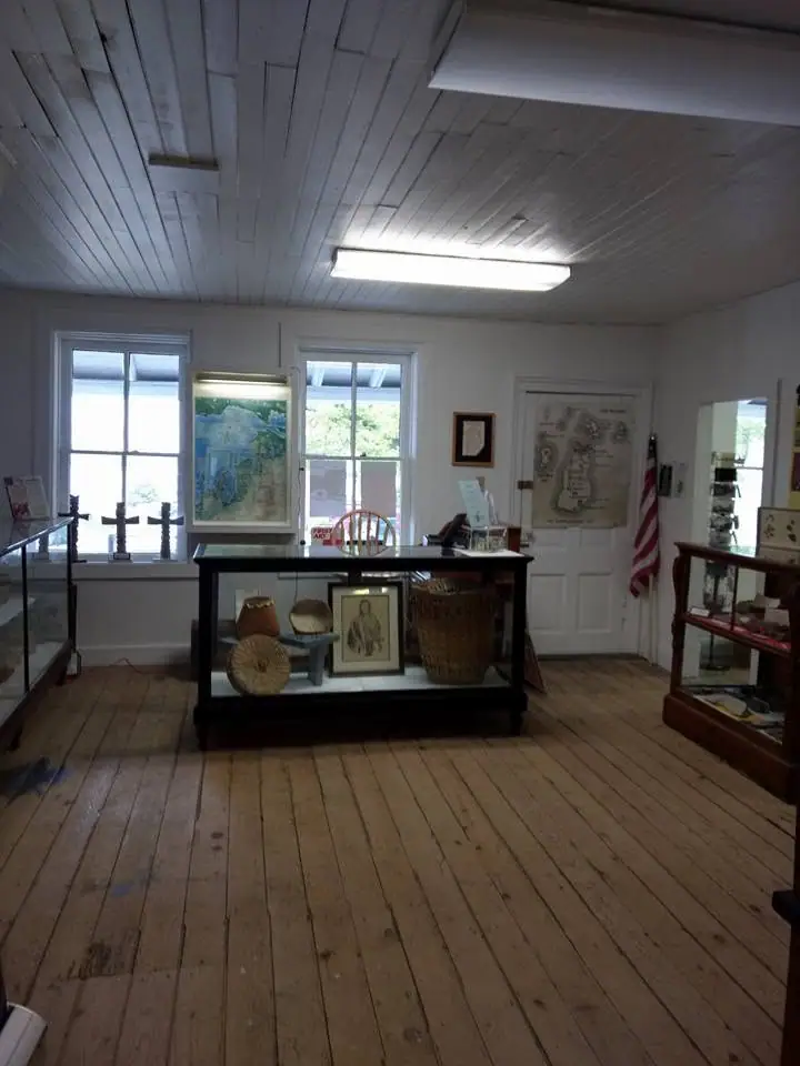 Interior of a small museum room with display cases, framed maps, artifacts, and an American flag.