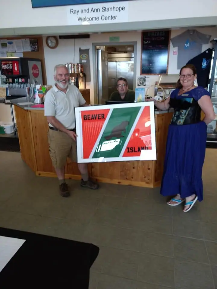Three people pose at a counter while holding a framed graphic inside a welcoming center.