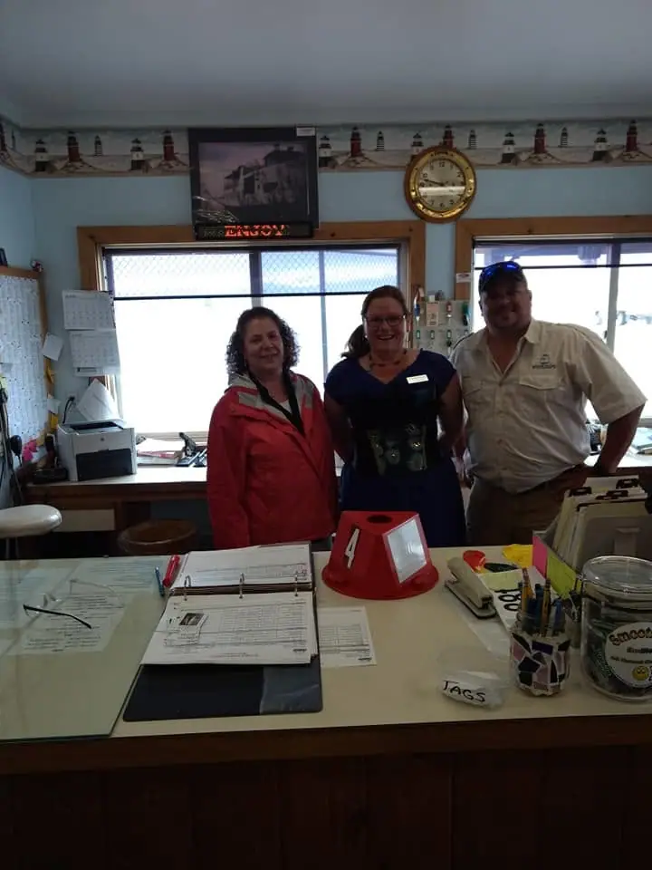 Three people pose behind a service counter in an office decorated with lighthouse imagery.