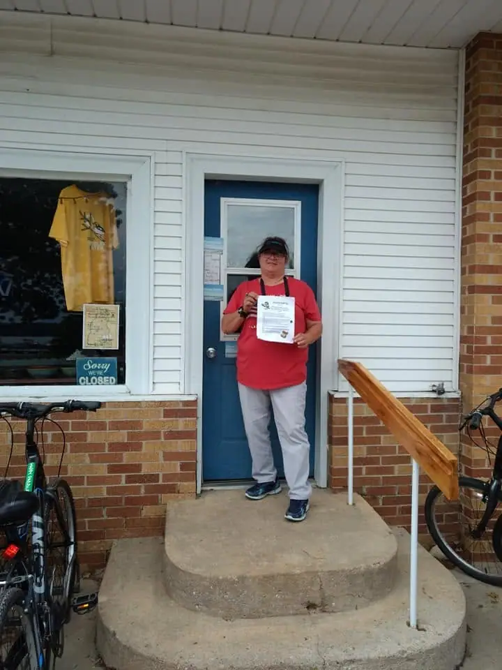 A person holds a printed document outside a blue door beside bicycles and a window sign reading “Sorry WE’RE CLOSED.”