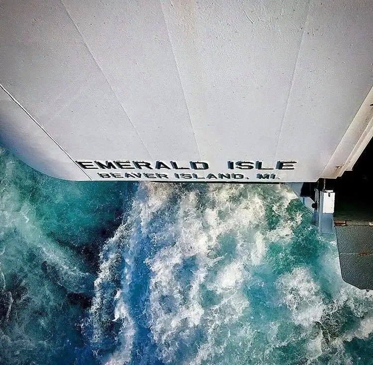 The stern of a ferry marked “EMERALD ISLE” cuts through churning blue water.